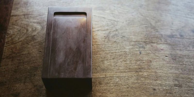 A rectangular dark stone inkstone with a recessed writing surface, resting on a sunlit wooden table
