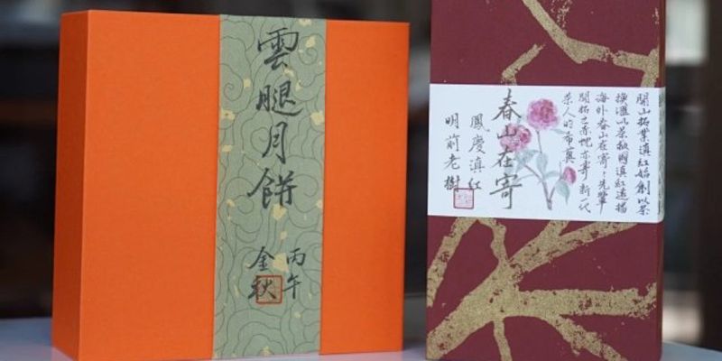 An orange box of Yunnan ham mooncakes with a green calligraphy band, standing beside a brick-red box of Dianhong tea