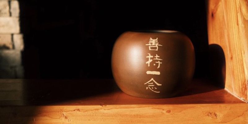 一只深色陶制水盂，刻有四字，被一束窗光照亮