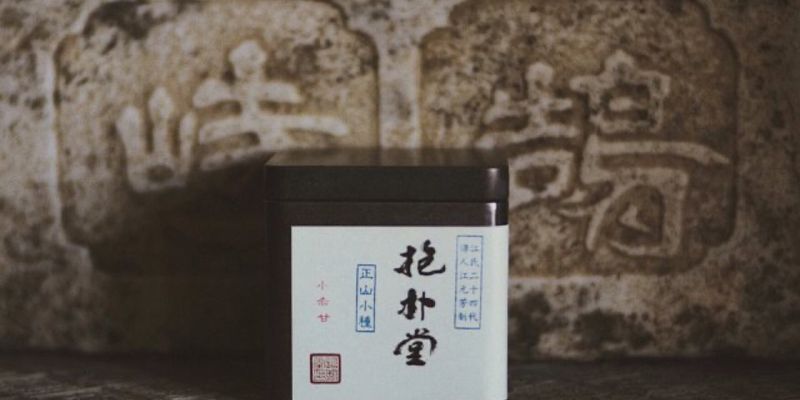 一个印有中文字样的深色茶叶罐,背景是一块带有大字雕刻的旧石碑