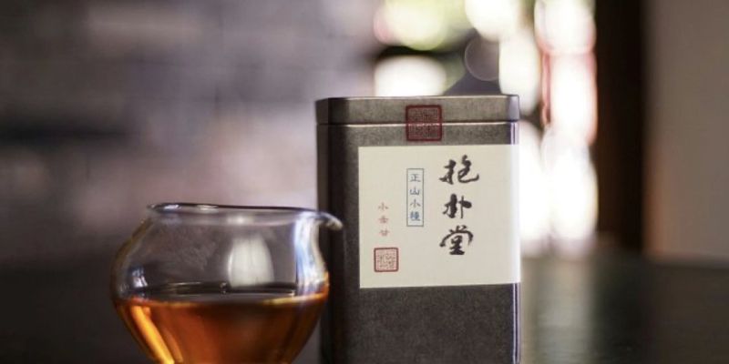 A glass of amber tea beside a tall tin labeled in Chinese, lit by soft window light