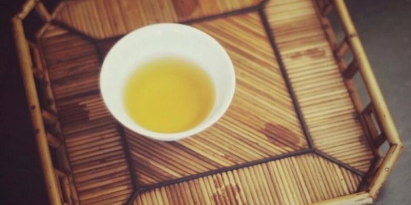 A white cup of golden tea resting on a woven bamboo tray