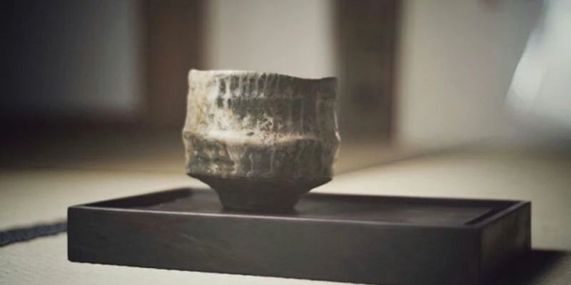 A rough-textured ceramic cup resting on a dark, flat stone tray inside a softly lit room