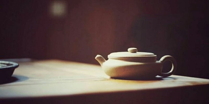 A flat, round-bellied unglazed clay teapot resting on a wooden table in warm afternoon light