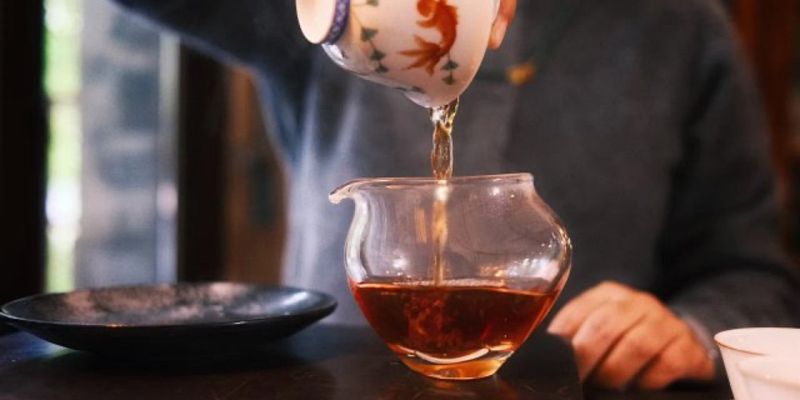 A white cup of golden oolong tea set on a square bamboo tray