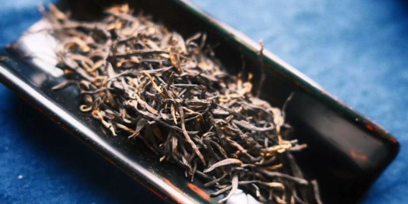 散落的深色金毫红茶干茶,铺在黑色托盘上,背景是蓝色布面