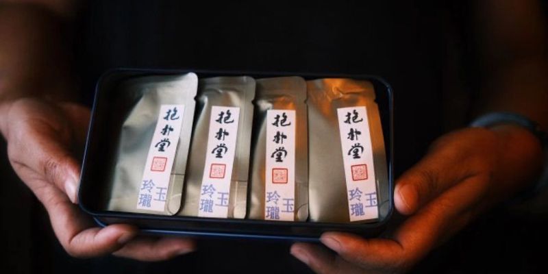 Two hands holding a tin box containing four foil-wrapped tea packets